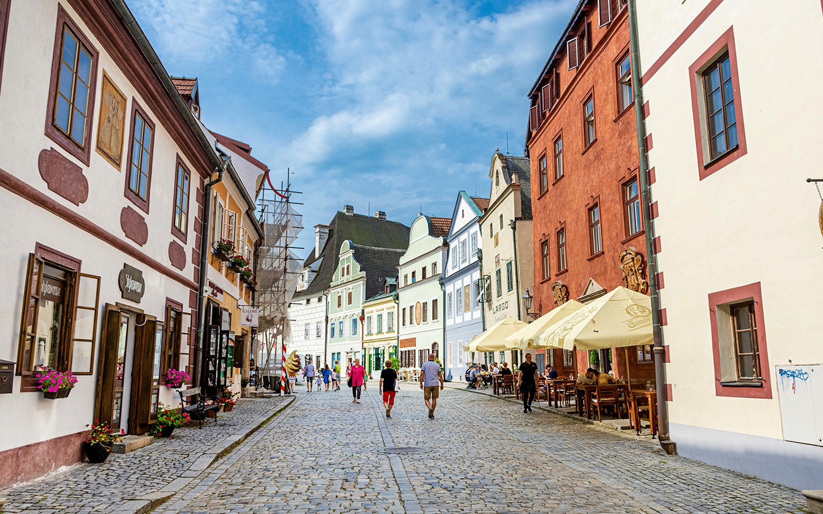 遊客在捷克克魯姆洛夫的一條鵝卵石街道上漫步，四周被色彩繽紛的歷史建築環繞。