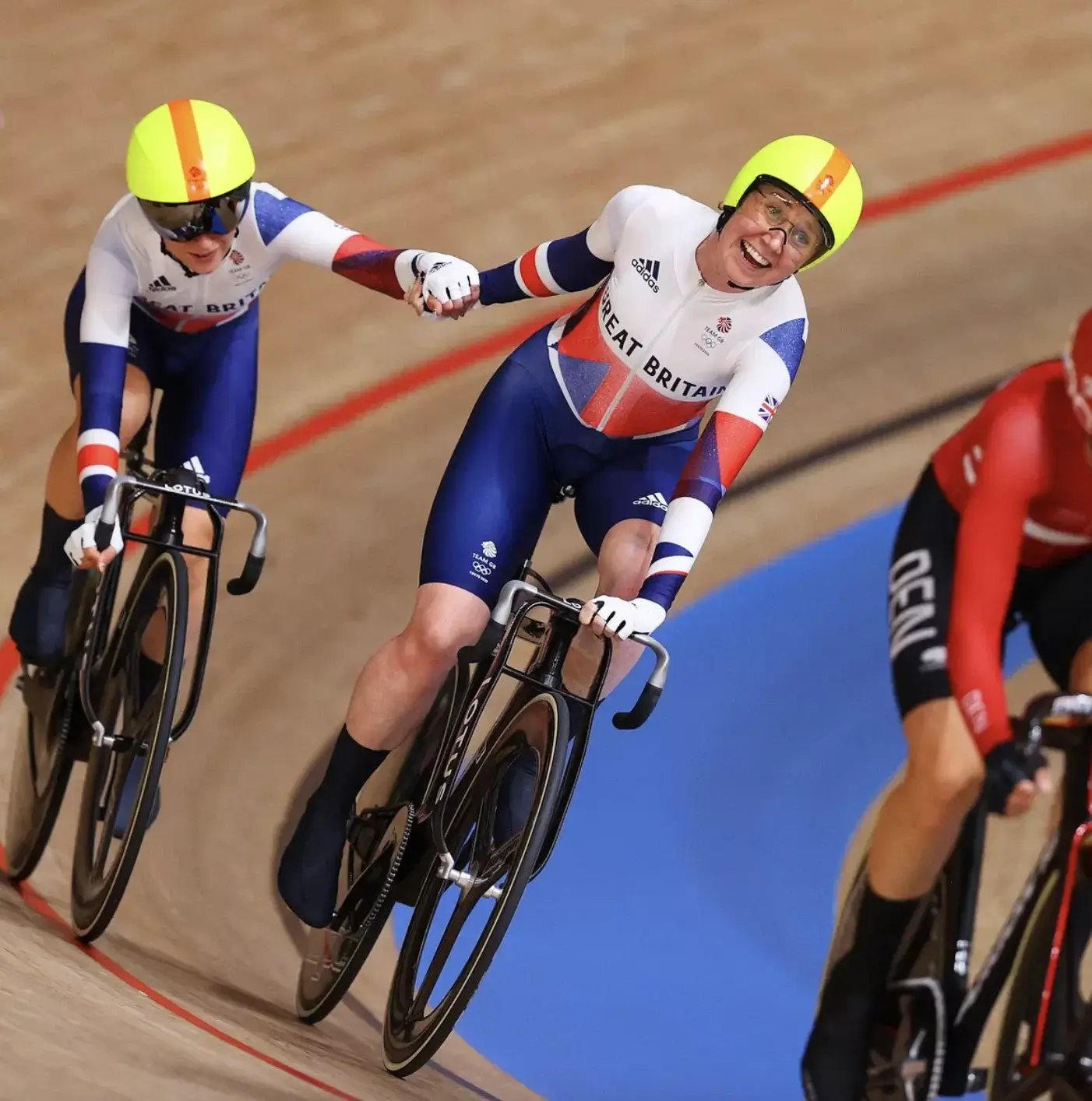Image of two British Olympic cyclists on a velodrome track holding hands.