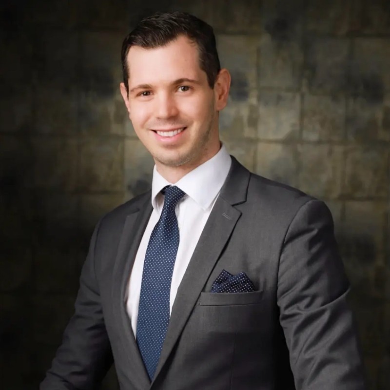 Man and woman standing together at a desk with a laptop and notebooks, smiling at the camera.