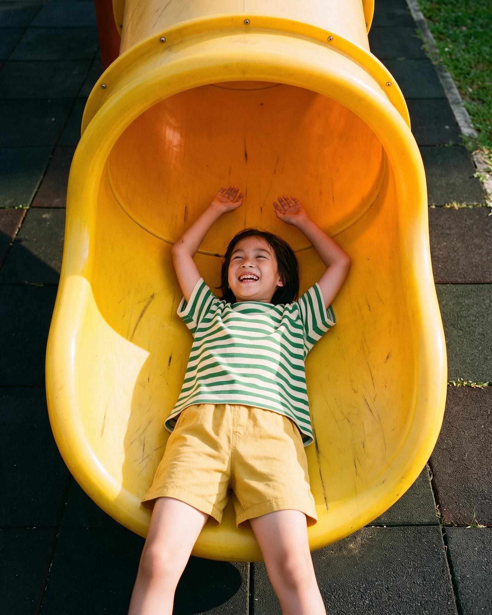 Smiling child enjoying a yellow playground slide.