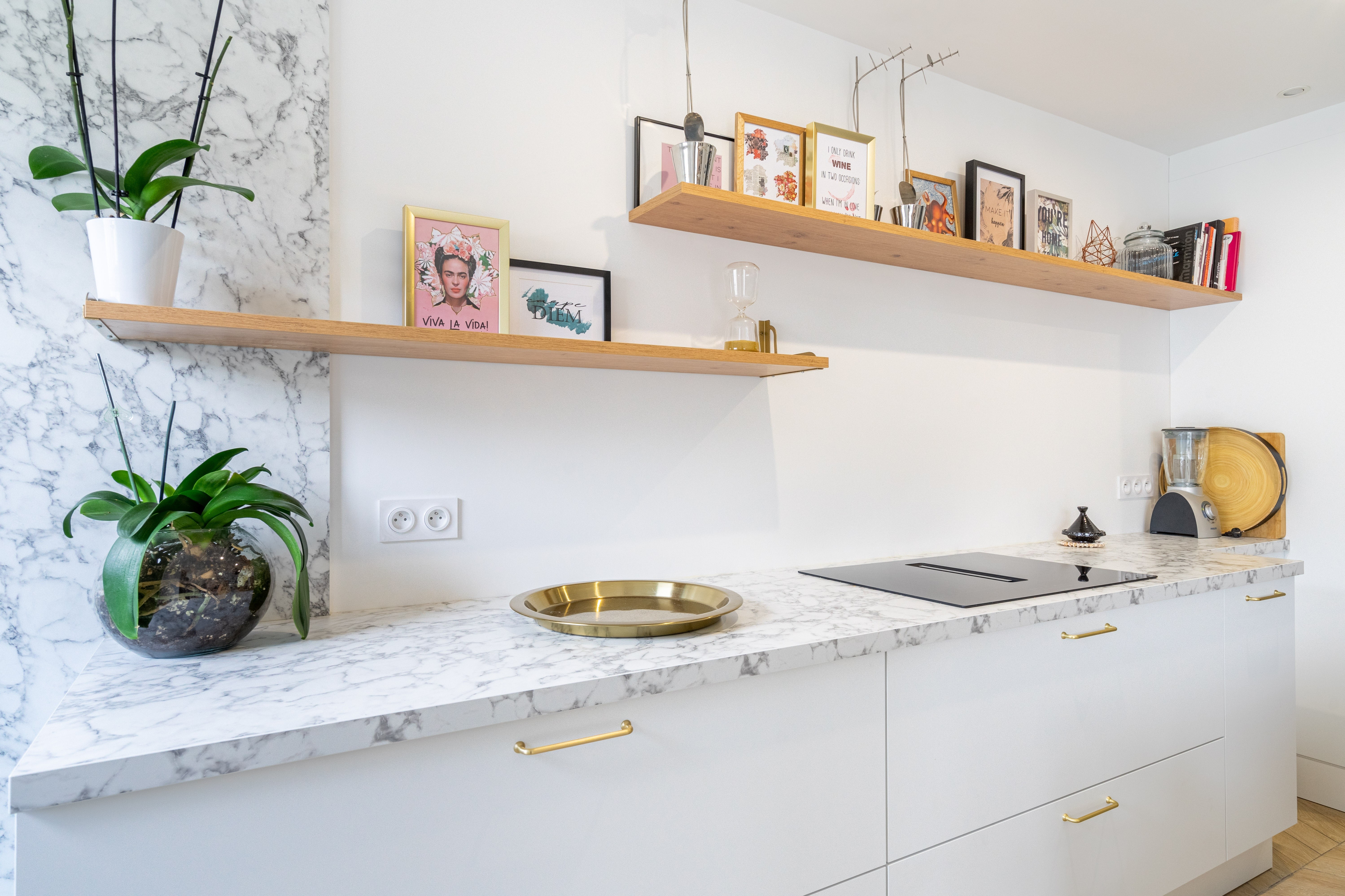 Transformation cuisine Seine-et-Marne avec plan travail marbre blanc, poignées dorées et étagères flottantes bois avec œuvres d'art, rénovation complète.