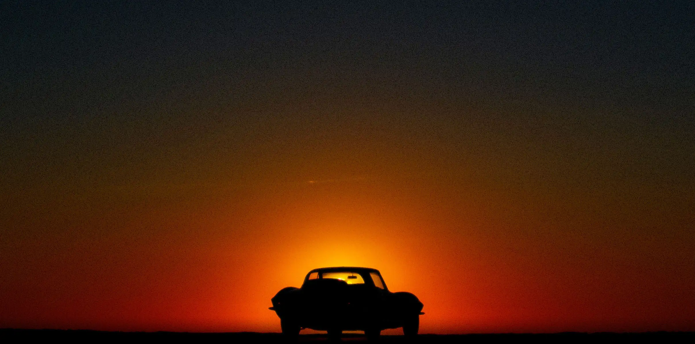 A red sports car parked in-front of a sunset.