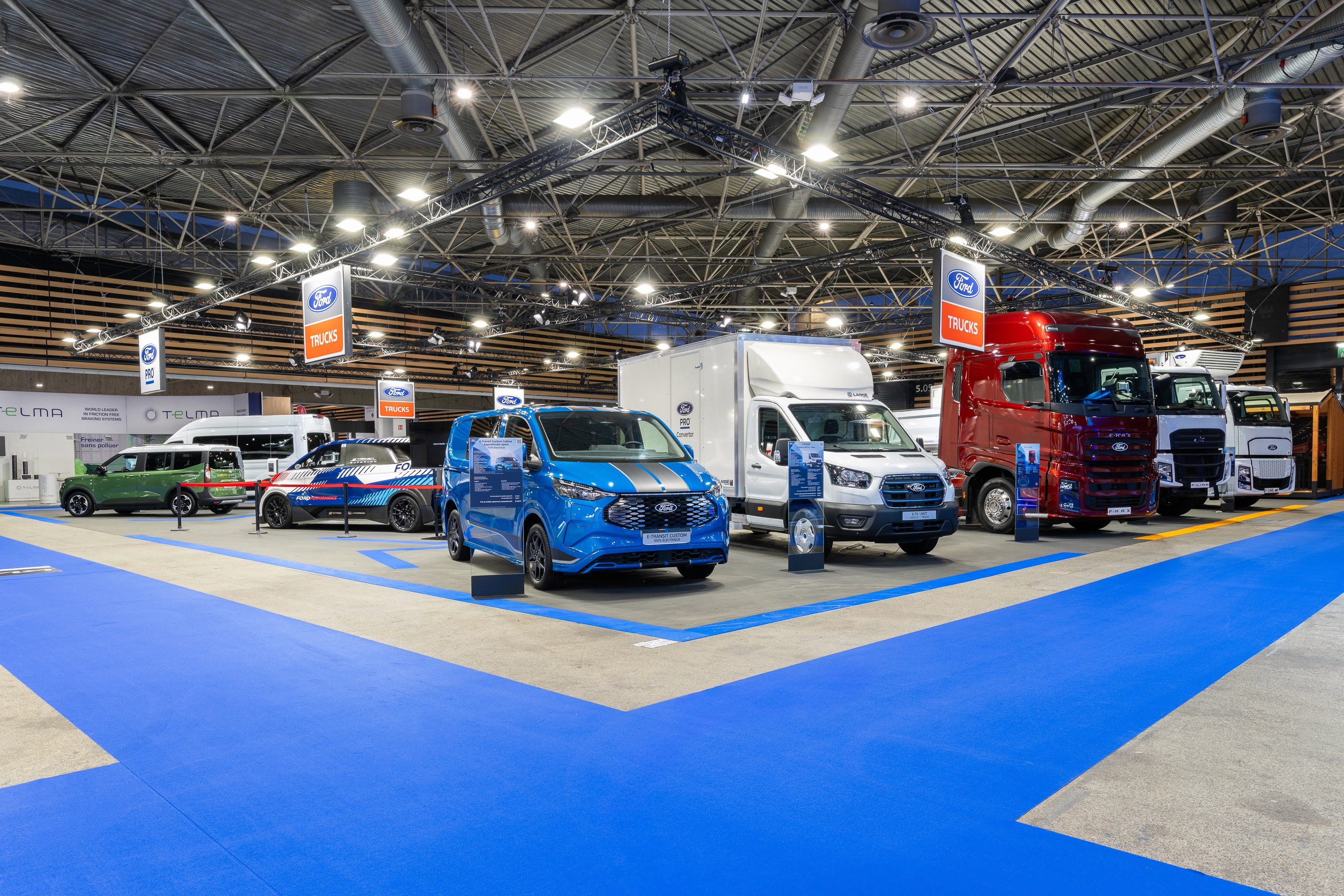 Stand Ford Trucks Solutrans Lyon 2026 réalisé par Expace – vue frontale avec poids lourds exposés sur sol bleu vif à marquages géométriques et signalétique de marque grand format