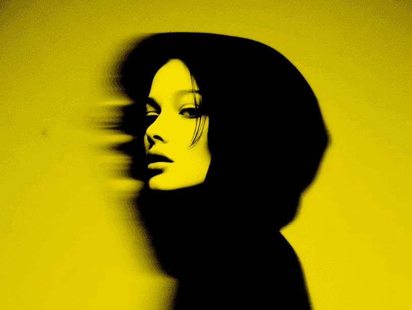 Figura femminile in silhouette nera su fondo giallo, con volto parzialmente sfocato dal movimento laterale.