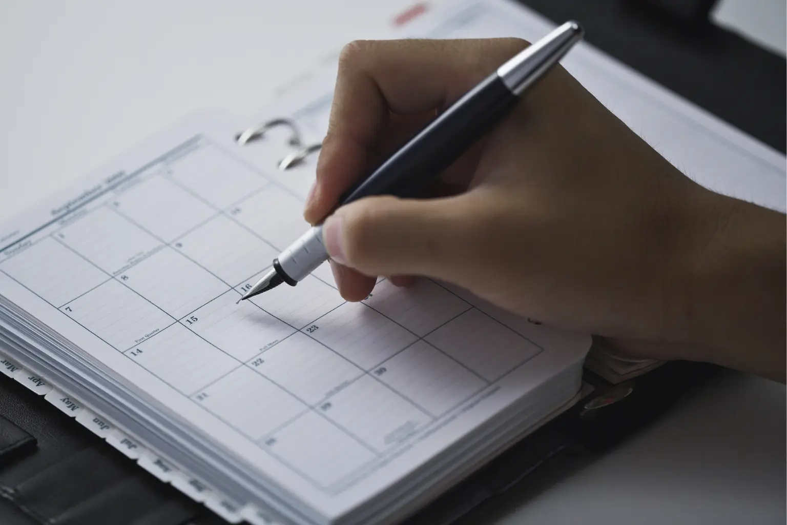 Custom scheduling automation showing a person writing in a planner with a pen on blank monthly pages.