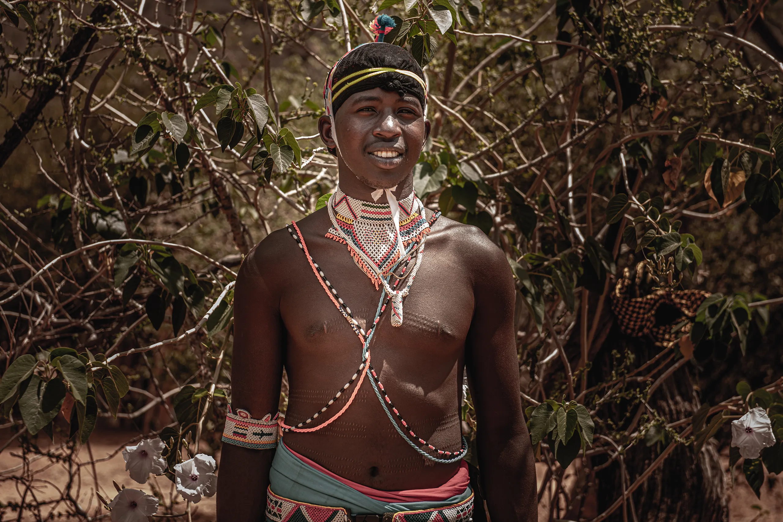 A close up portrait of a Samburu man wearing traditional red and white beaded jewelry and headwear.