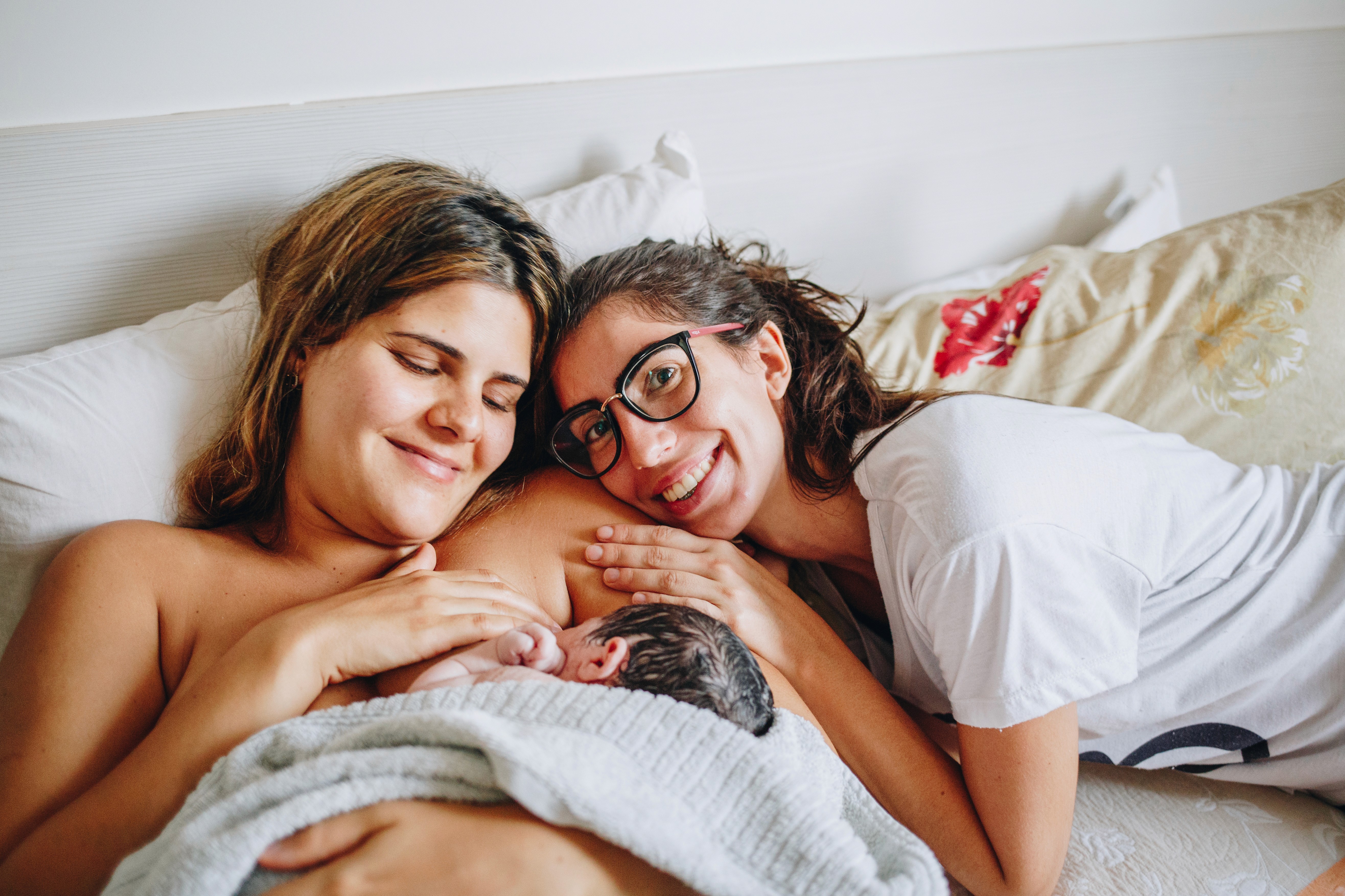 mãe com o filho nos braços e uma doula deitada em seu ombro