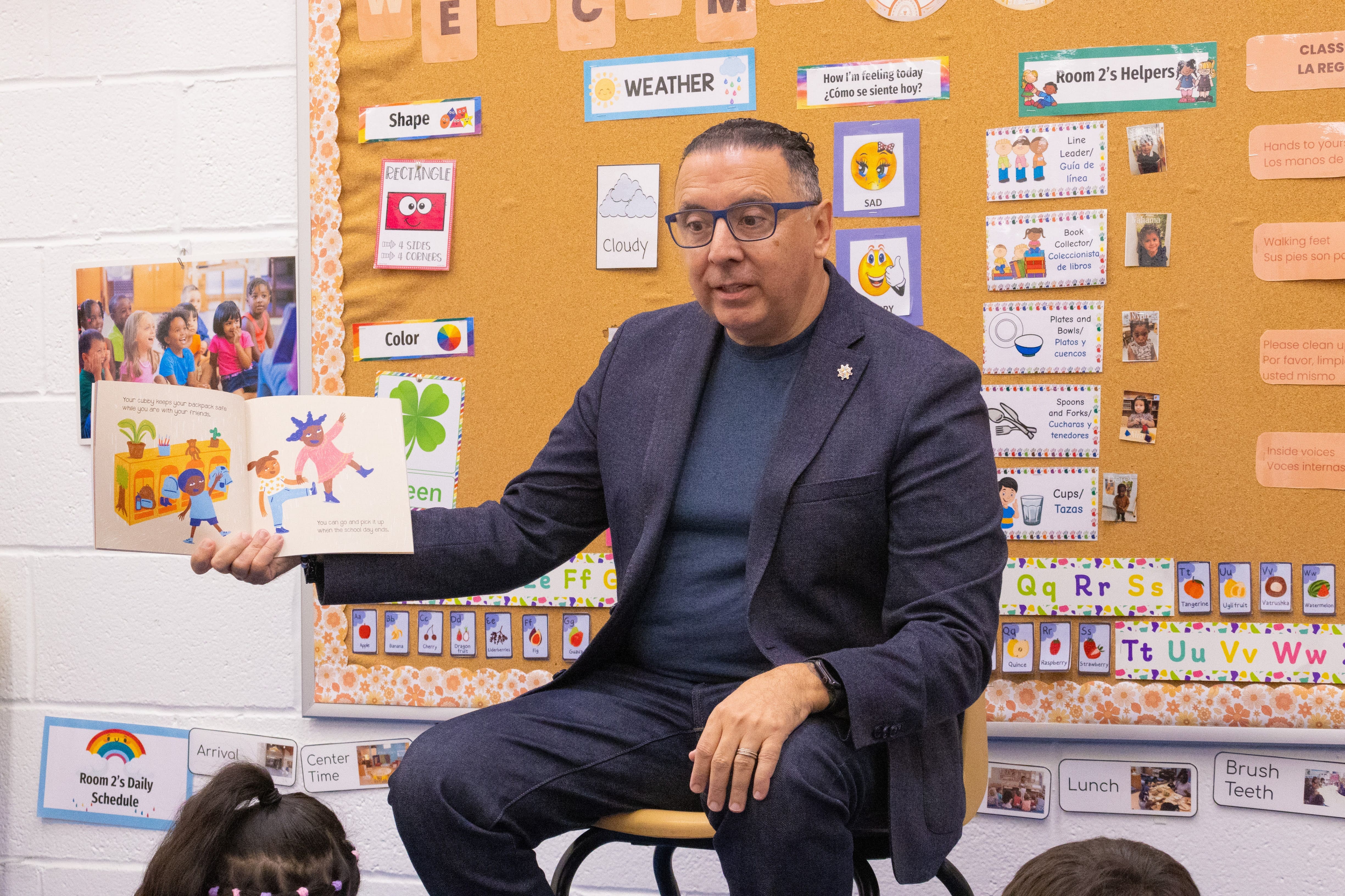 A man wearing glasses reads a book to young children