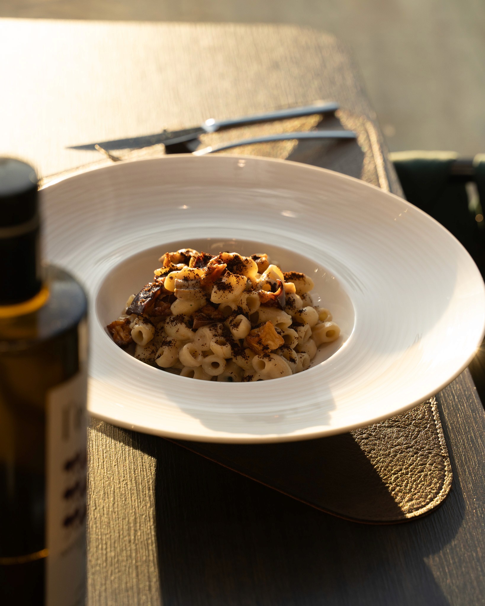 „Teller mit cremiger Pasta, verfeinert mit gebratenen Pilzen und Gewürzen, serviert im warmen Abendlicht auf einem gedeckten Restauranttisch.“