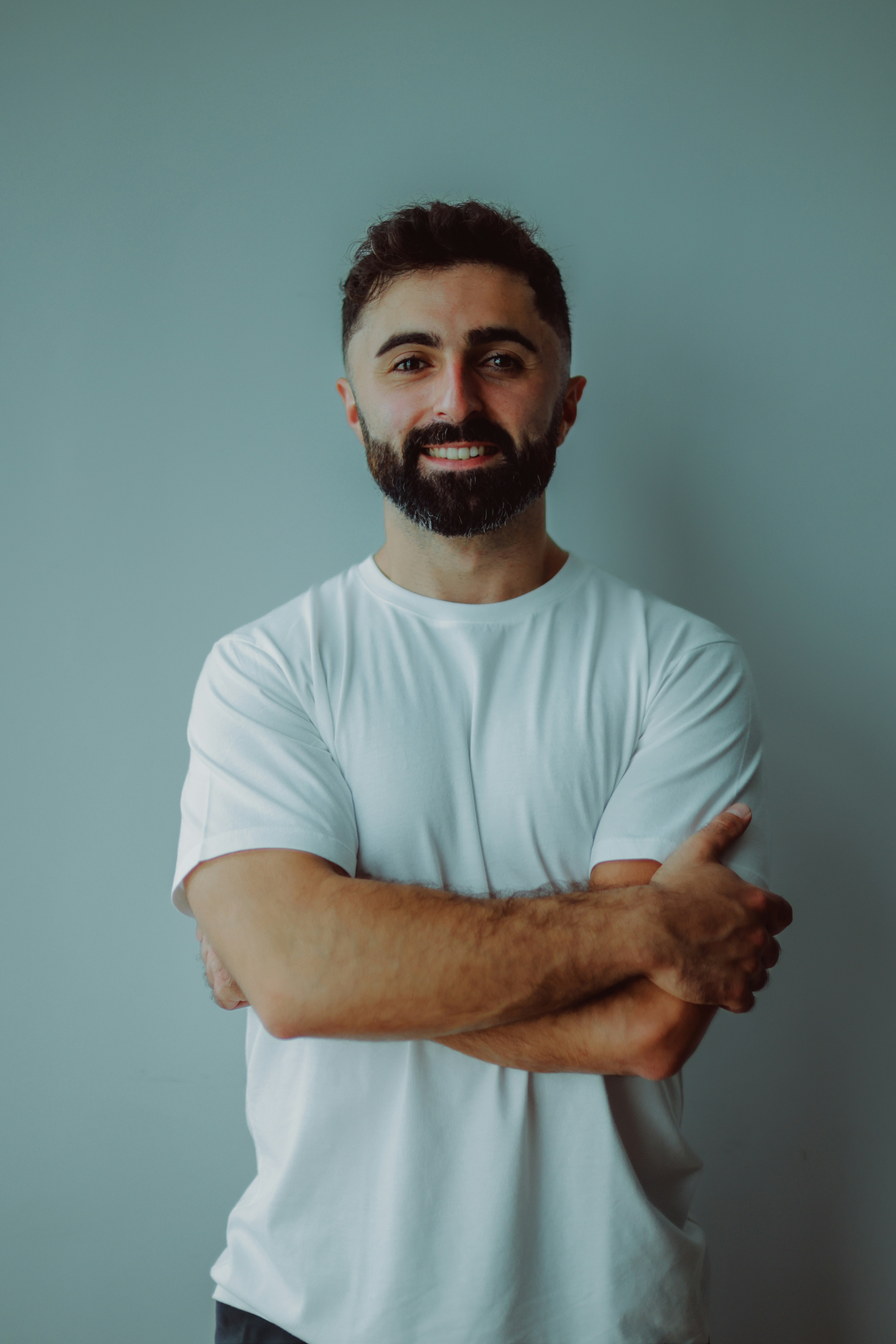 A smiling man with a beard wearing a white t-shirt