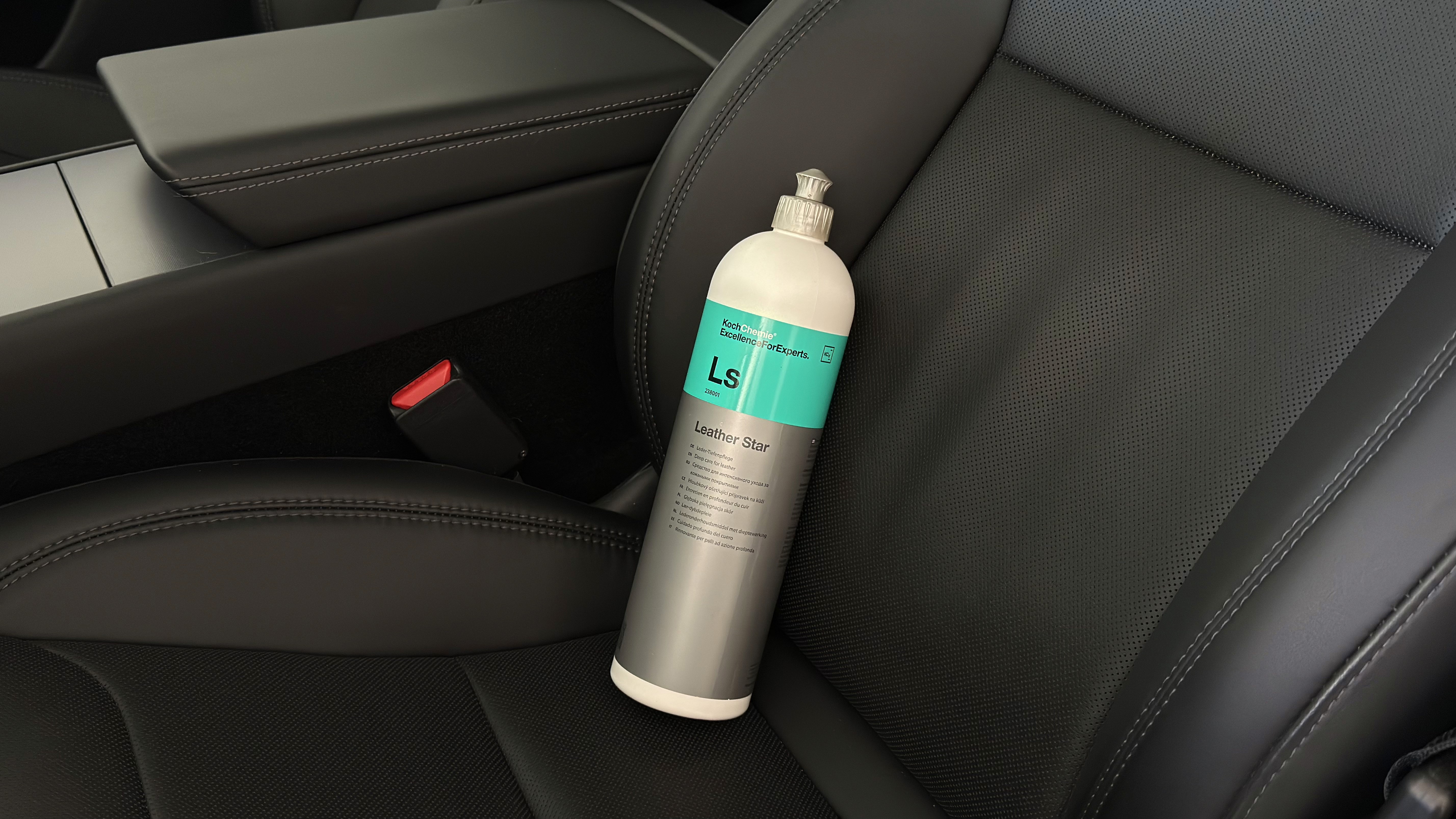 Bouteille de produit Koch Chemie Leather Star posée sur un siège en cuir noir d’une voiture, avec console centrale et boucle de ceinture rouge visibles à côté.