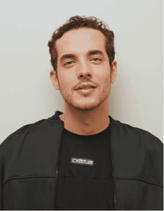 Retrato de um homem jovem com cabelo castanho curto, barba rala e jaqueta preta sobre camiseta preta, em fundo claro.