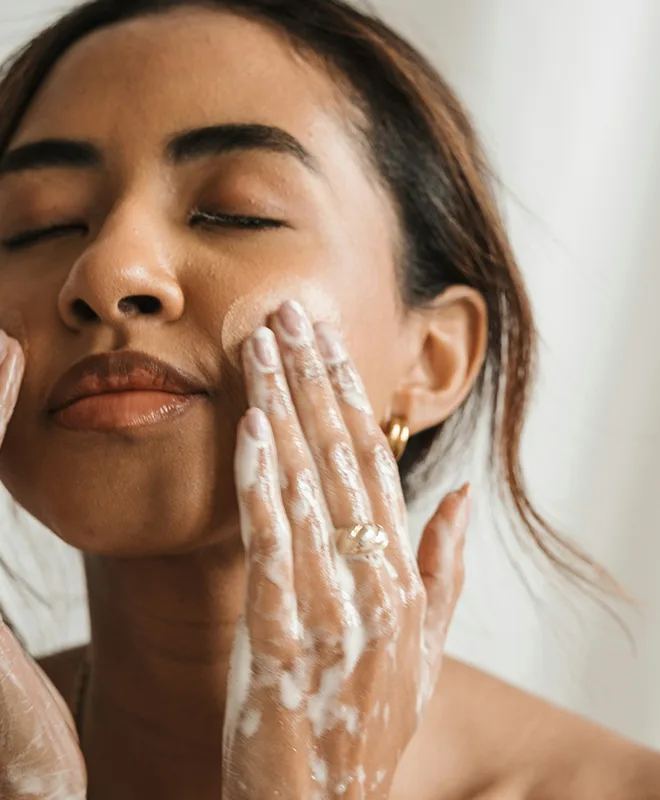 A woman with closed eyes gently washing her face with a foamy cleanser
