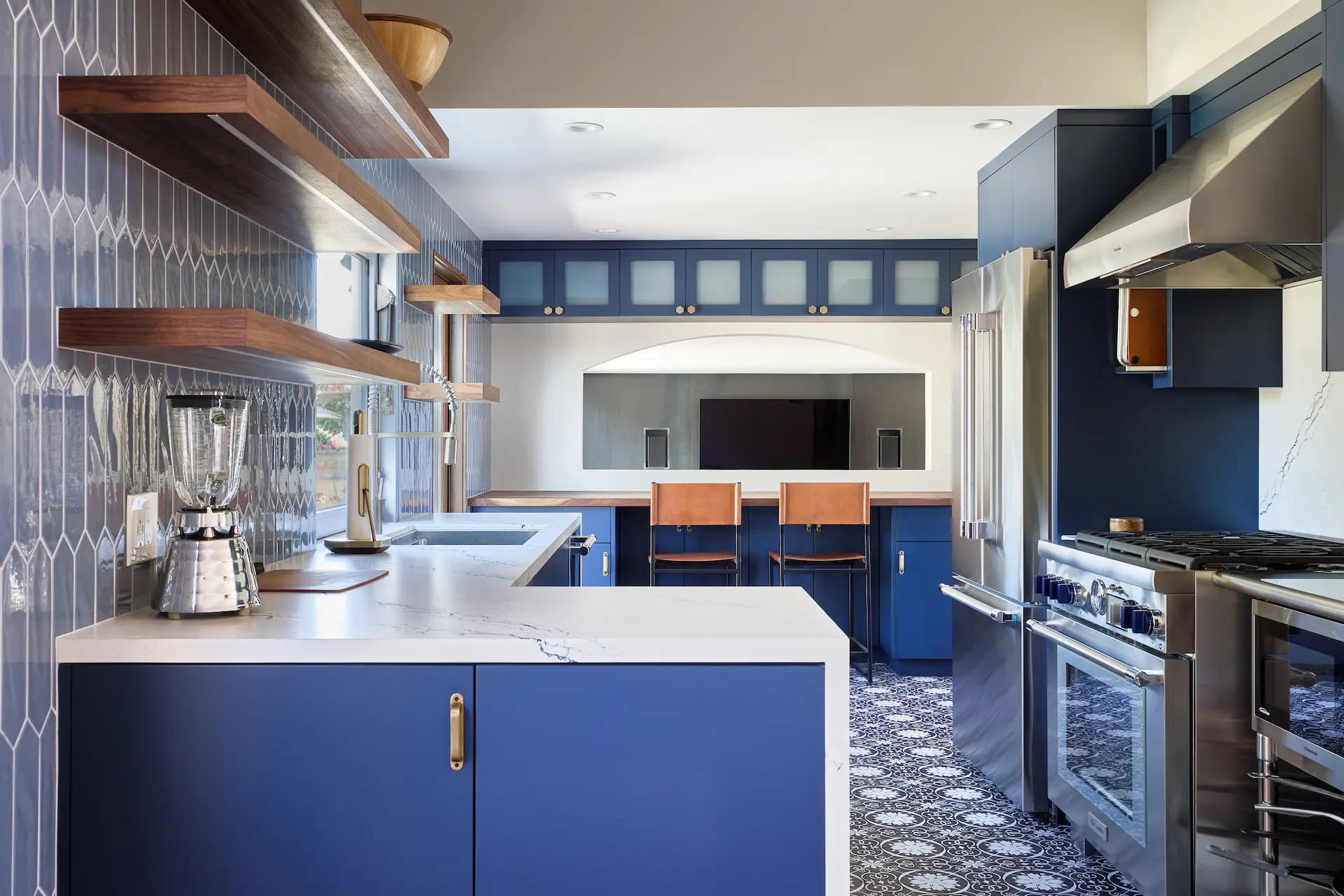 Wide shot of the entire modern transitional kitchen, focusing on the butcher block countertop bar seating with tan leather chairs, set against blue flat-panel cabinetry with antique brass hardware in the Huntington Beach Kitchen project. Photo by Todd Huge.