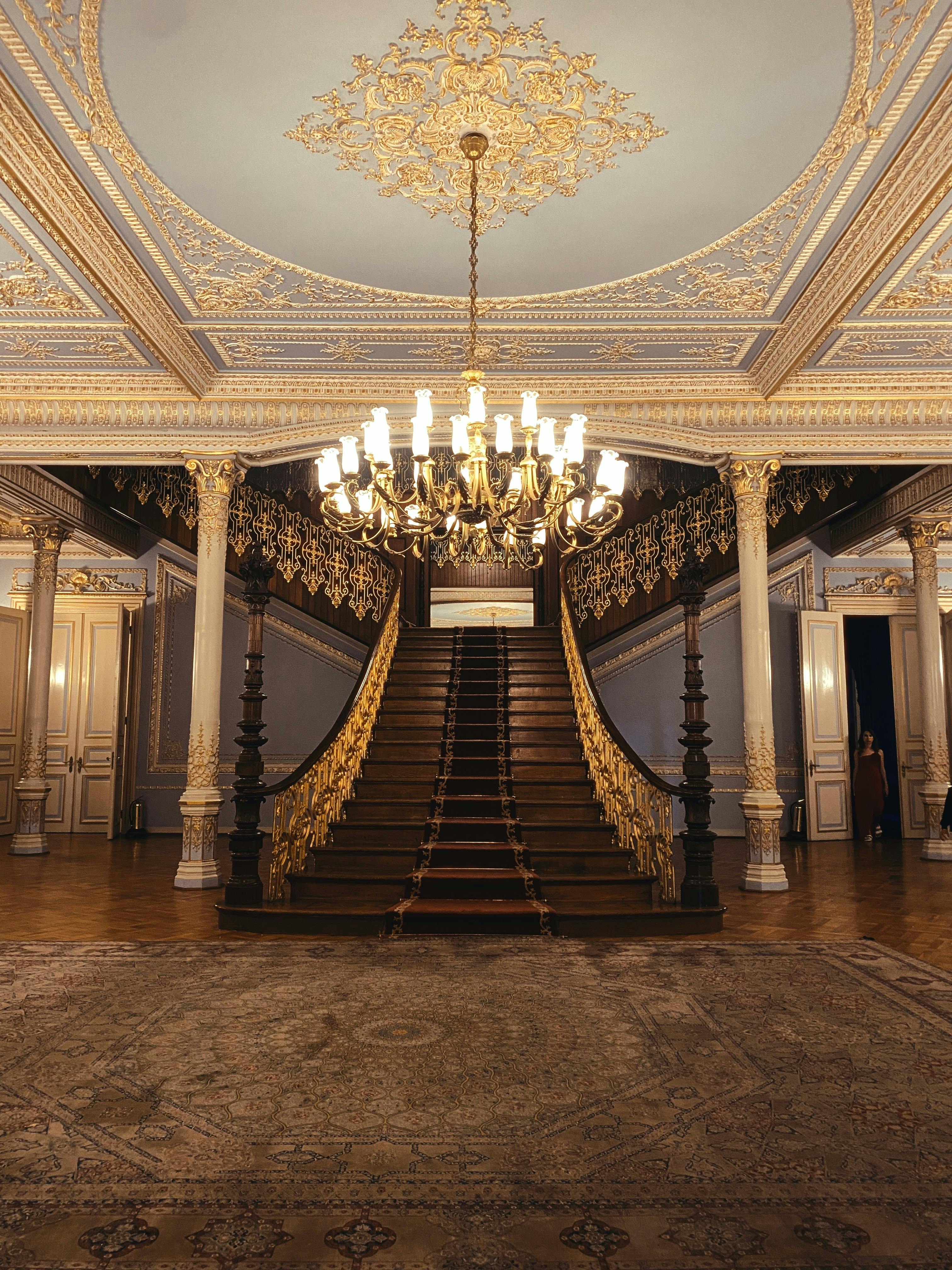 A fully traditional white-themed room with floral styling, a piano, a mirror, and a large chandelier.