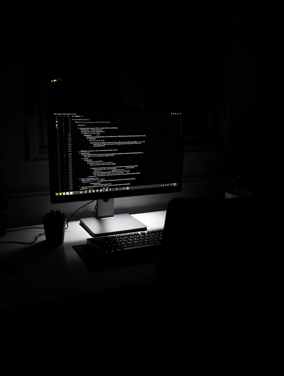 Computer monitor displaying lines of code on a desk in a dark room.