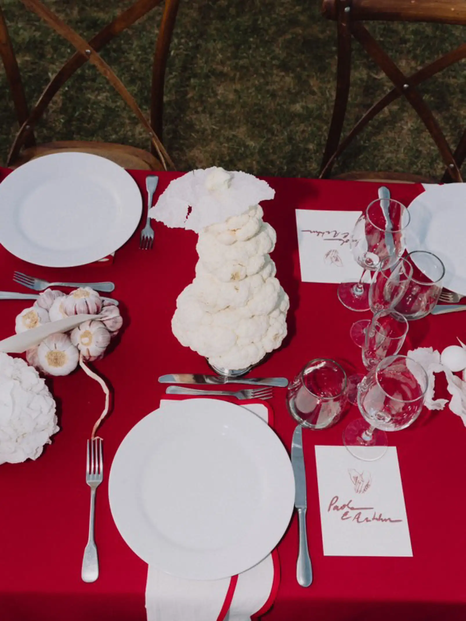 Mesa con mantel rojo y composición artística de coliflores y ajos para producciones florales que exploran el equilibrio entre arte, naturaleza y gastronomía.