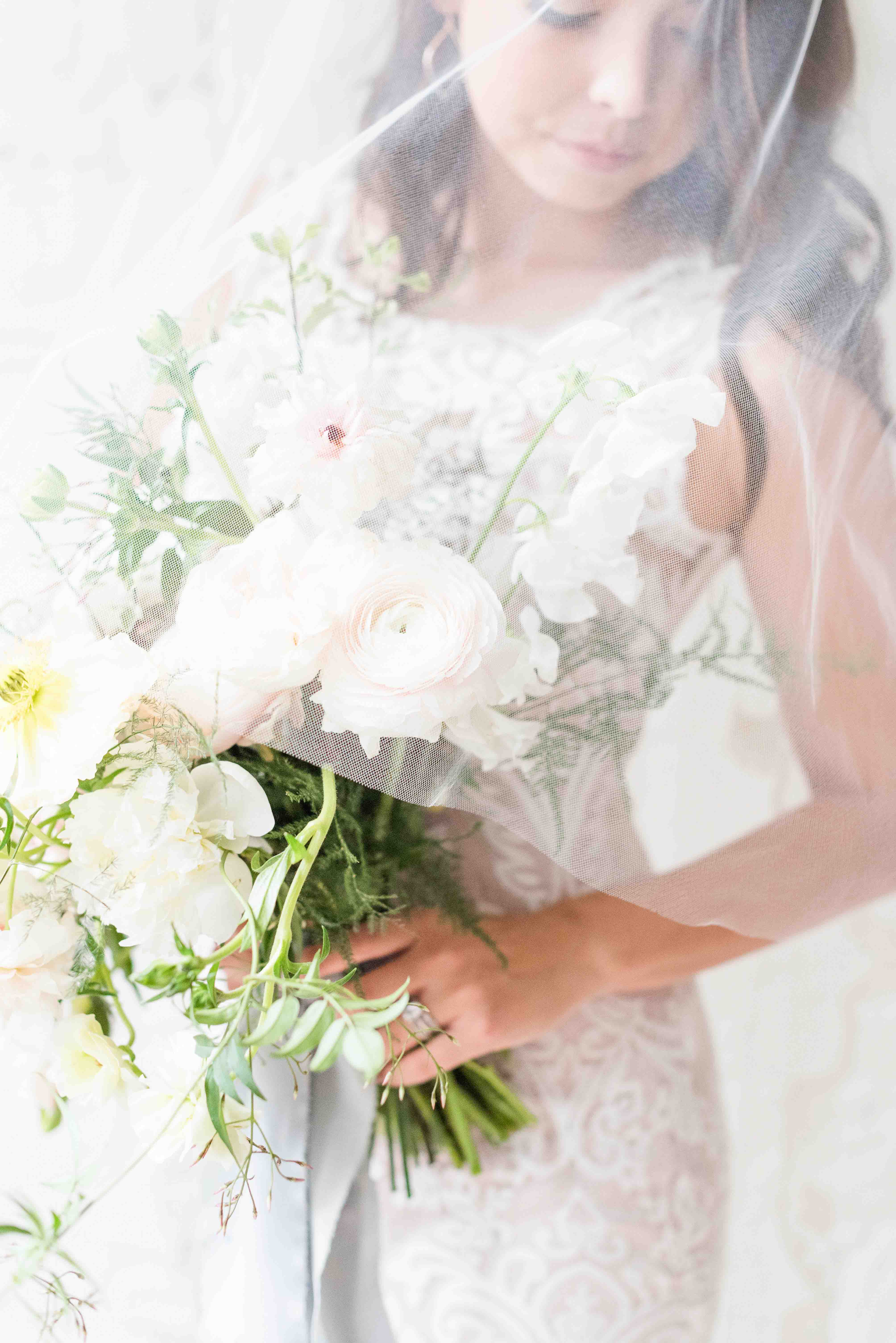 Image of bride holding a floral bouquet with the veil over her head.