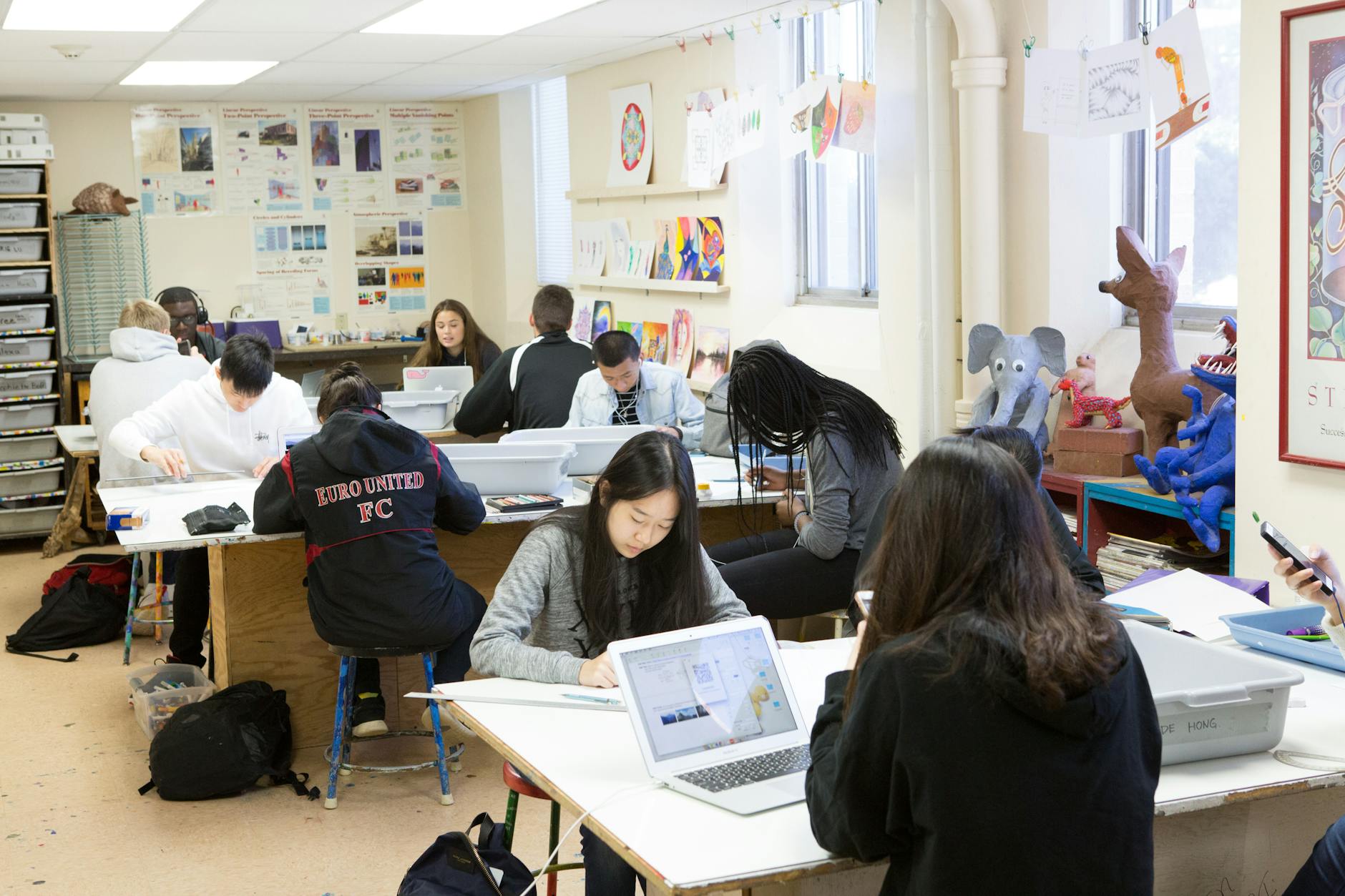 High school students collaborating on a coding project using laptops and a shared monitor in a modern classroom.