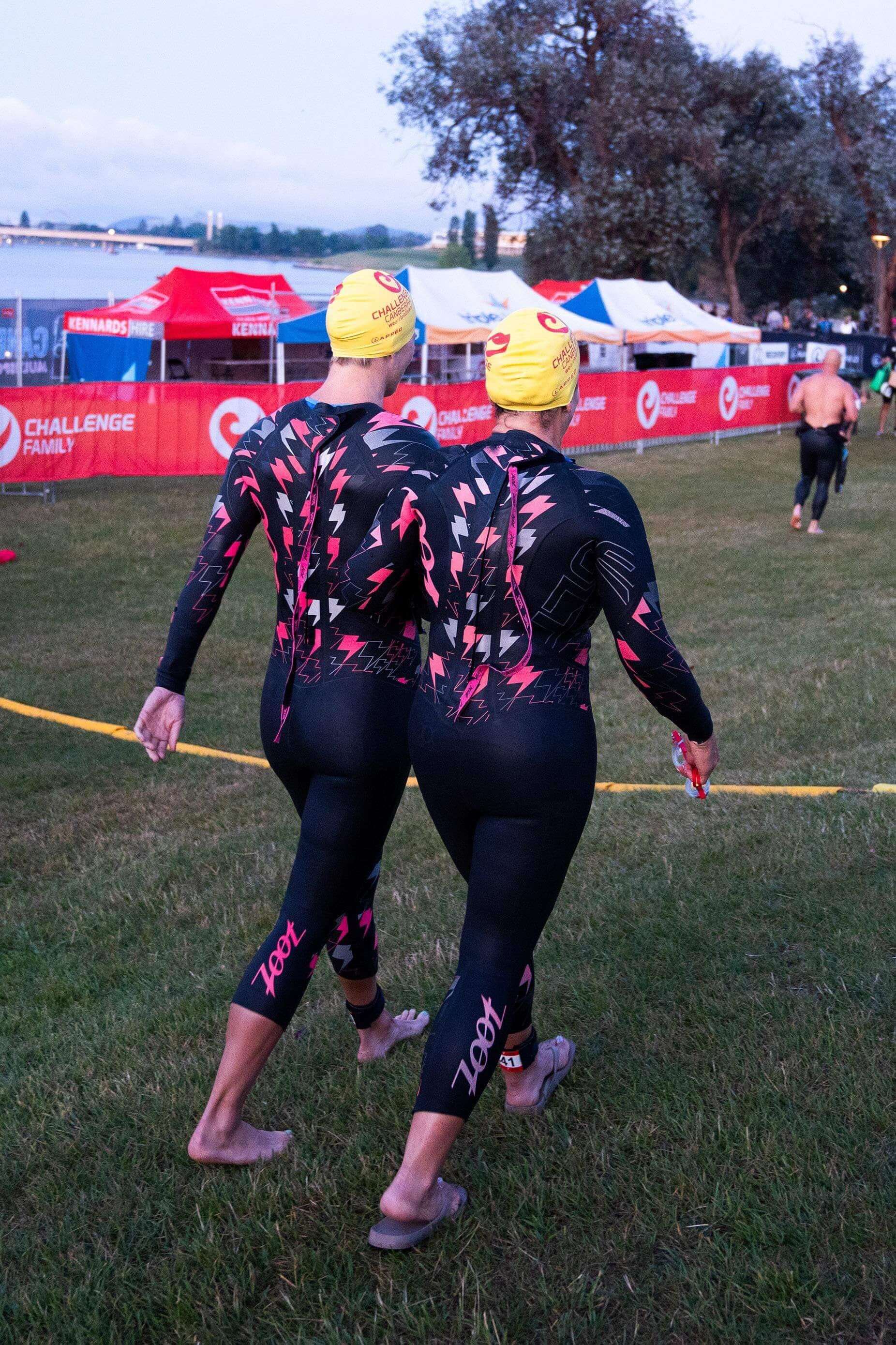 Lily and Jay in swimming kit walking towards the start line of the Canberra challenge swim. Lily is tethered to Jay from the thigh with a swim tether.