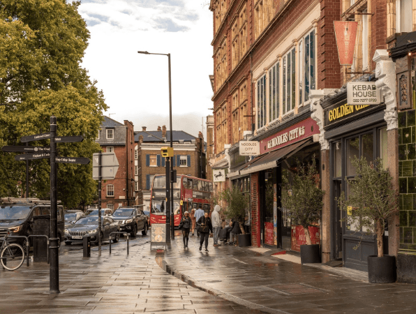 A smiling man with curly hair is sitting at a desk, looking at the camera, with a laptop and a lamp in the background.