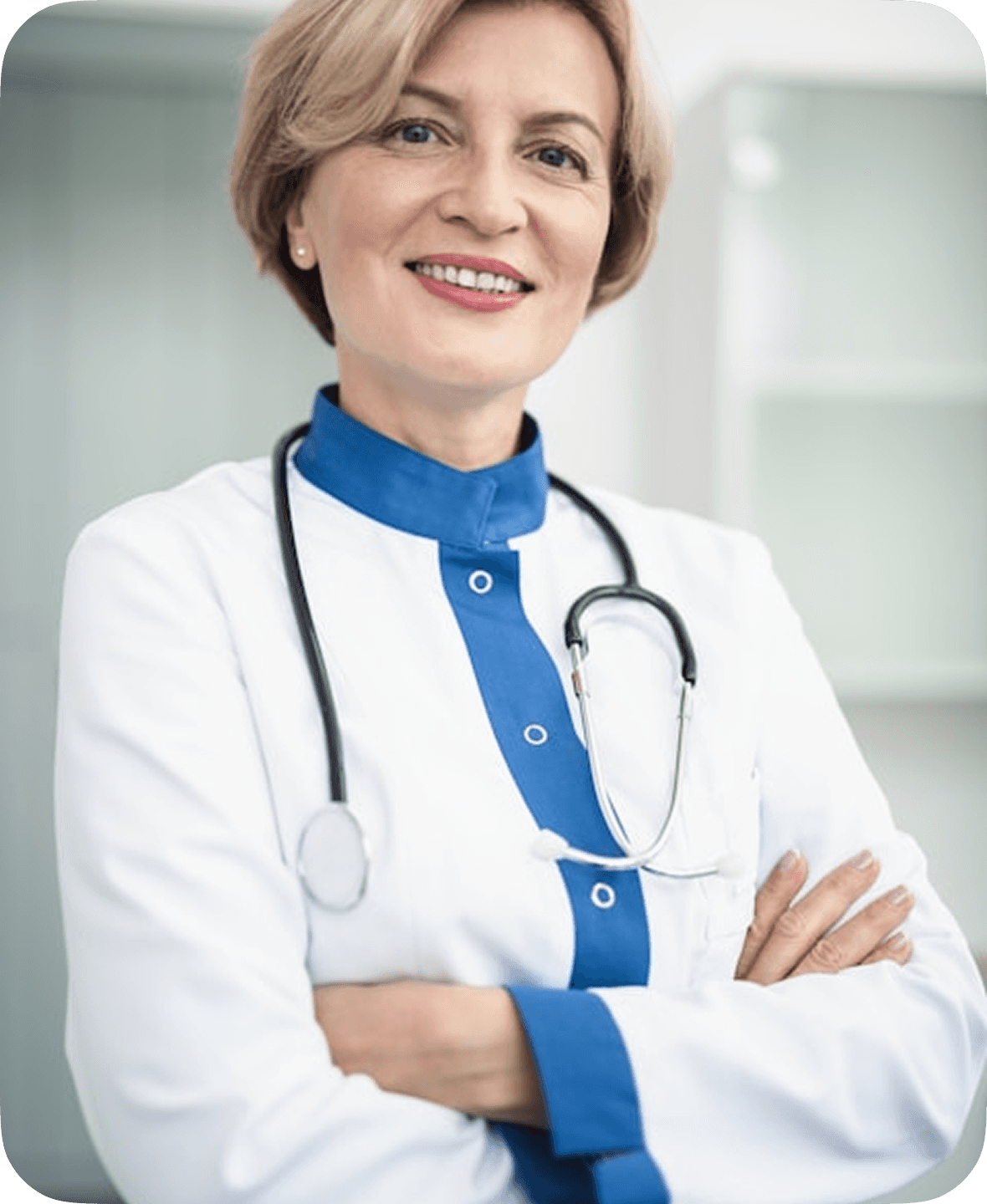 A confident female doctor in a white and blue medical coat stands with arms crossed, wearing a stethoscope around her neck, in a bright, clinical setting.