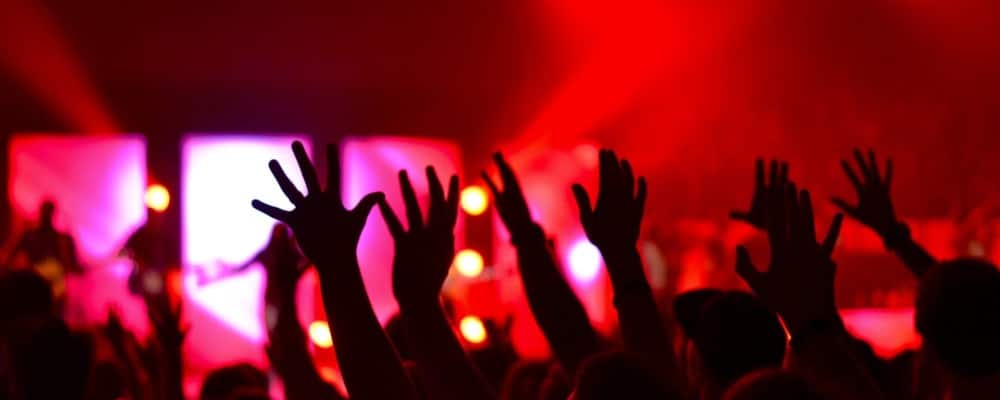 Concert crowd with raised hands under red lights.