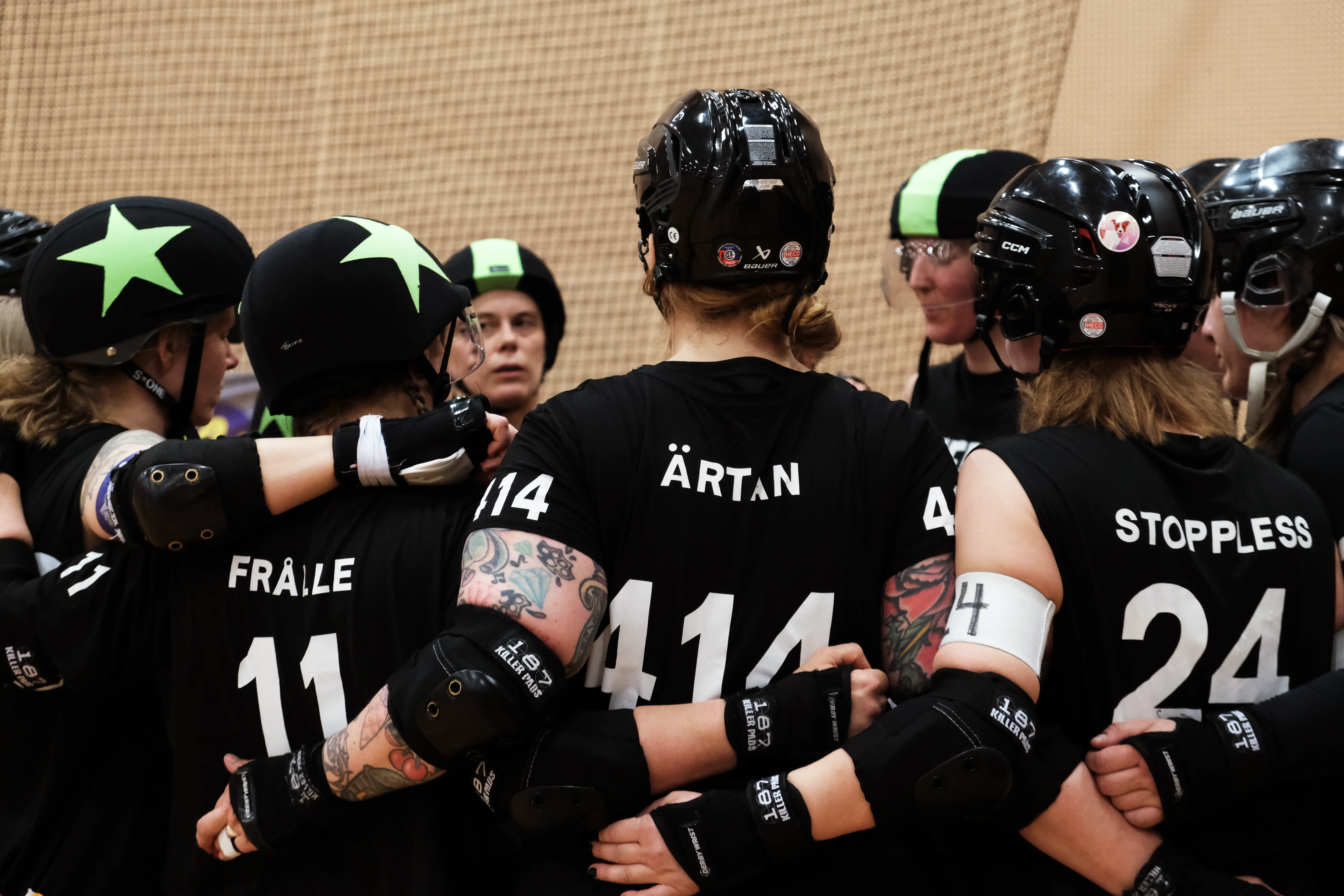 A group of roller derby standing in a circle, holding each others backs.