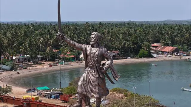   <img src="sindhudurg-statue-url.jpg" alt="Shivaji maharaj statue sindhudurg holding a sword stands near a tranquil bay surrounded by lush palm trees and coastal structures.">