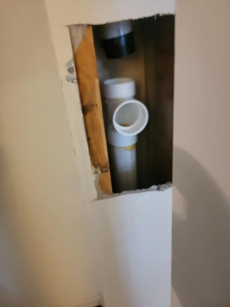 A section of drywall removed to expose white PVC plumbing pipes during a targeted residential pipe replacement.