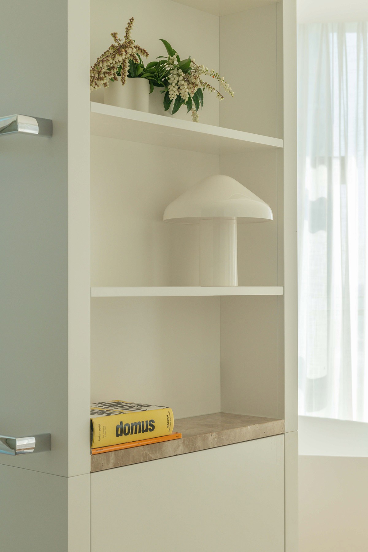 High Tide apartment interior styling detail with built-in shelving, sculptural lamp, greenery, and refined coastal finishes.