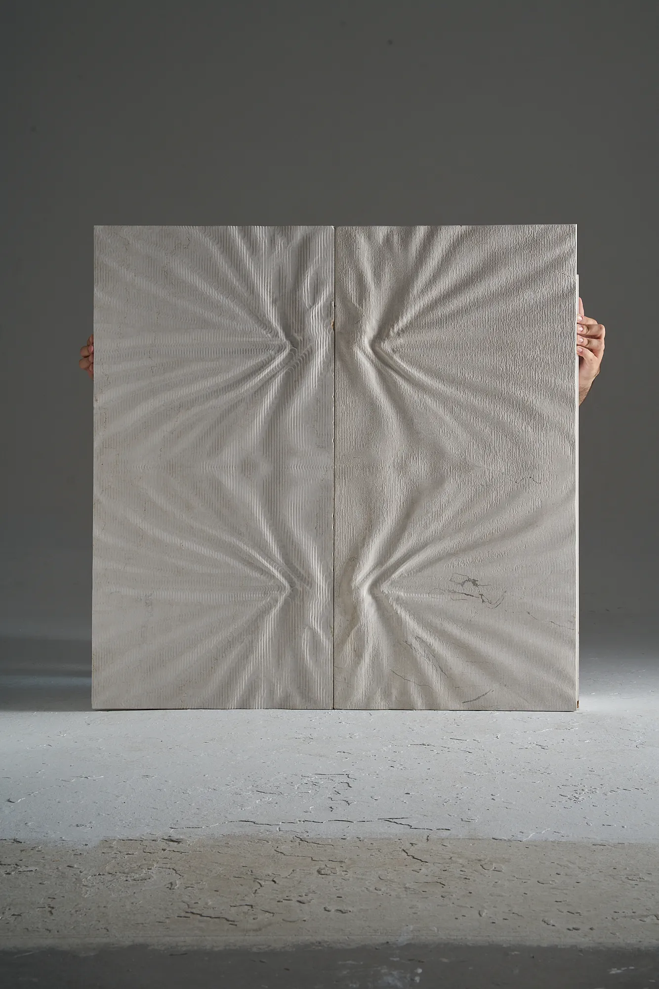 Front view of two large Curtis marble relief panels held for scale, showing their fabric-inspired surface patterns