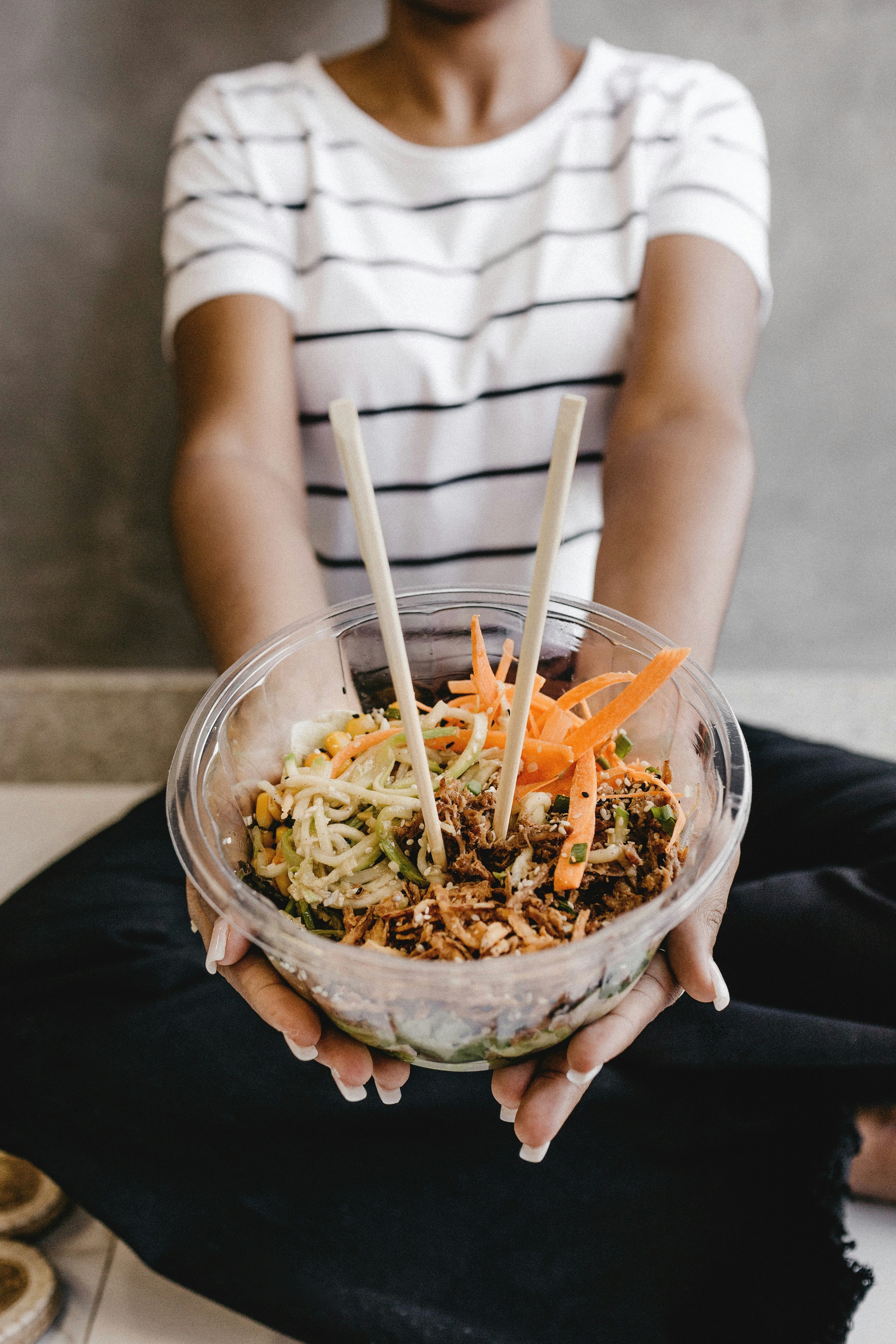 A smiling woman with her arms crossed, standing against a dark green background. She has long, dark hair.