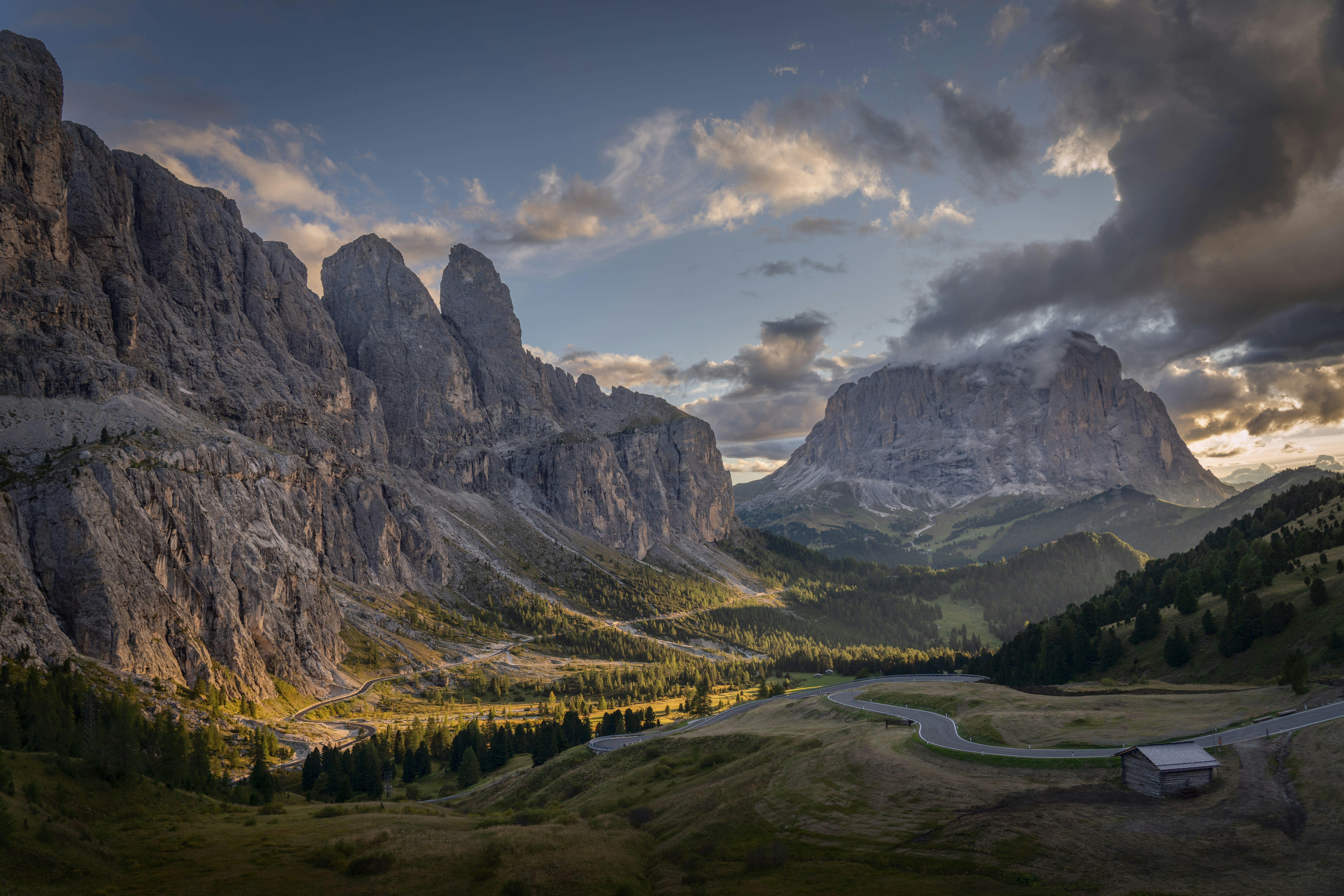 Dramatic mountain valley with a winding road and cabin.