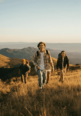 Grupa młodych dorosłych z uśmiechami na twarzyspacerujących podczas zachodu słońca z widokiem na góry