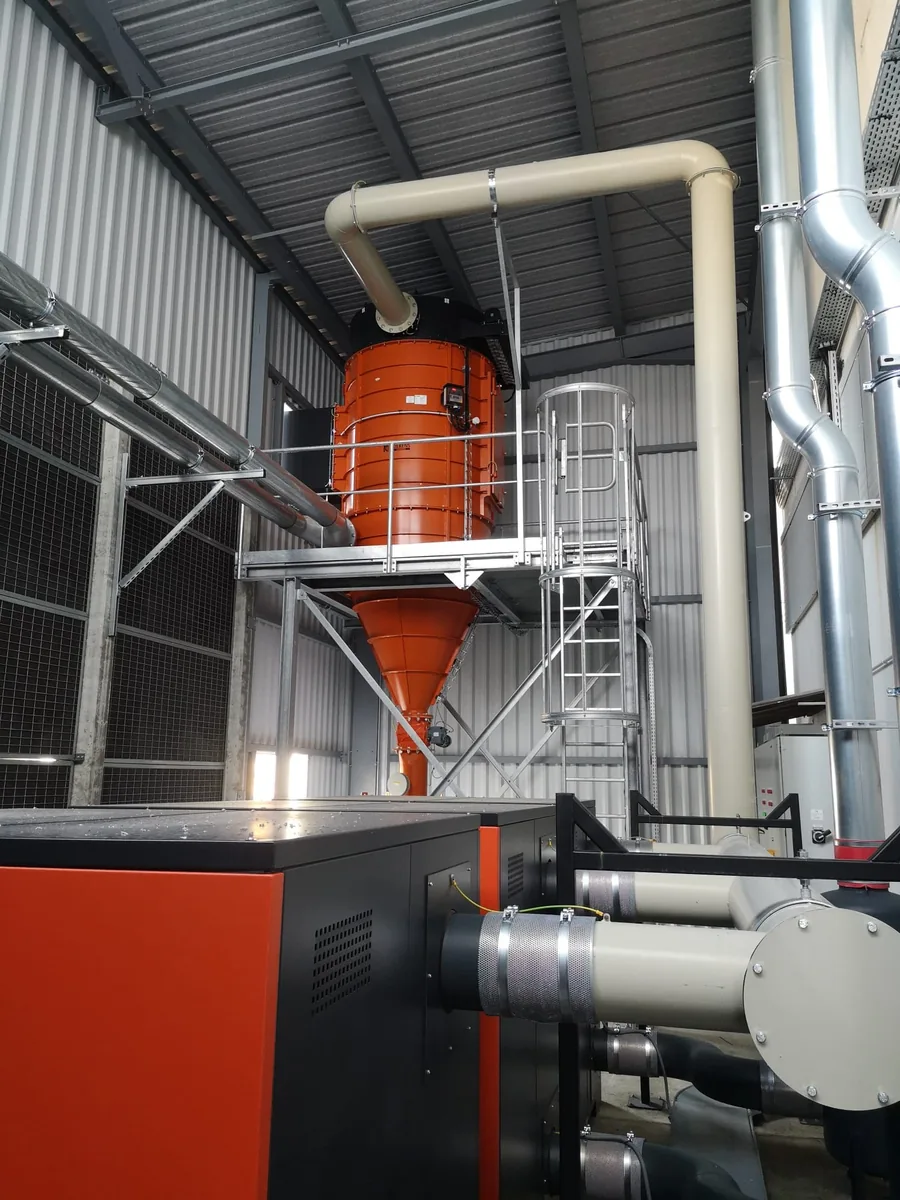 Cyclone orange installé dans un atelier, avec passerelle d’accès et tuyauterie reliée aux équipements d’aspiration industrielle.