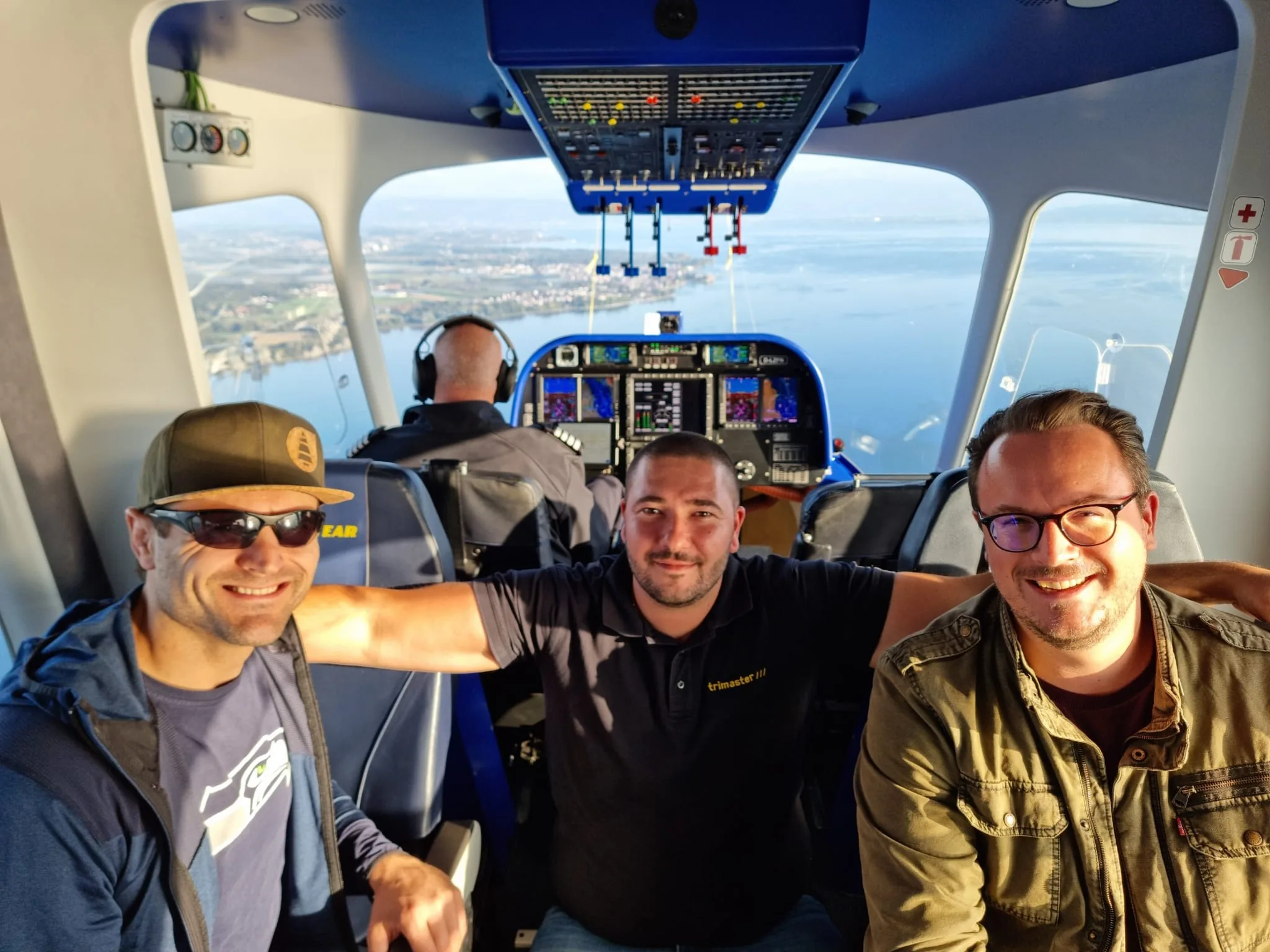 Drei Teammitglieder mit Headsets in der Kabine eines Zeppelins mit Blick über den See