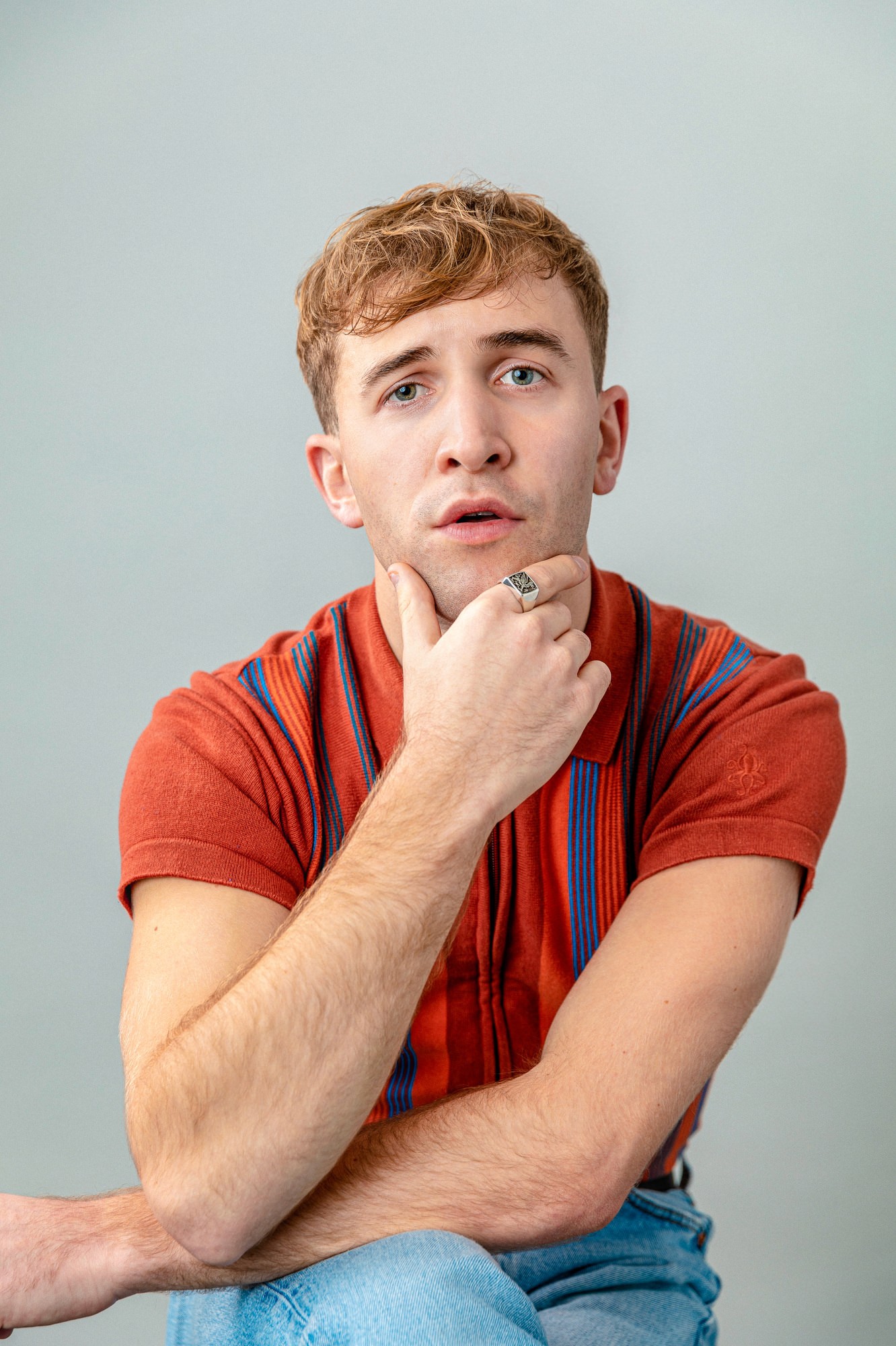 A young person in a red shirt rests their chin on their hand, looking thoughtfully at the camera.