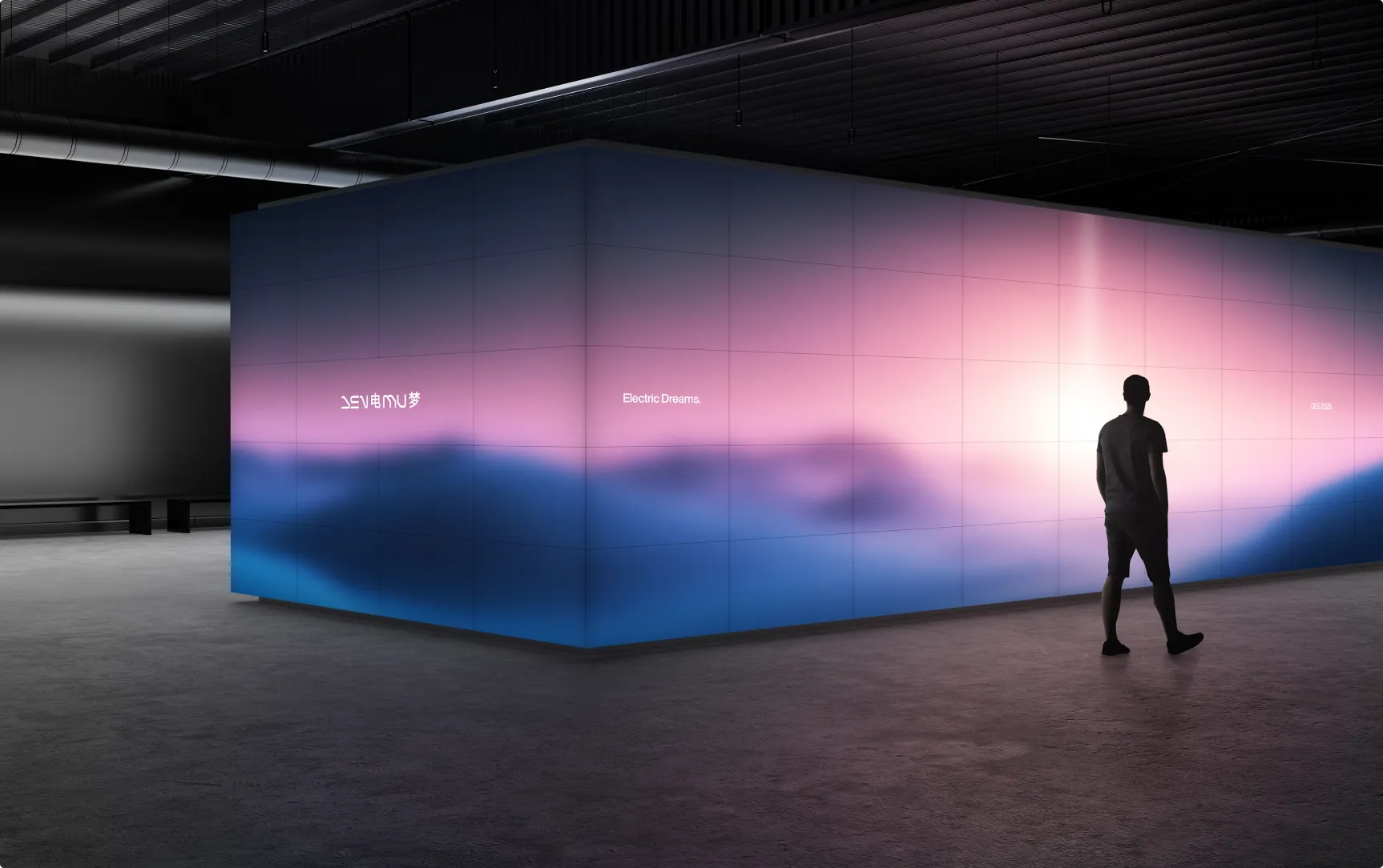 A person stands near a large, colorful wall projection with soft gradients of pink and blue in a dimly lit space.