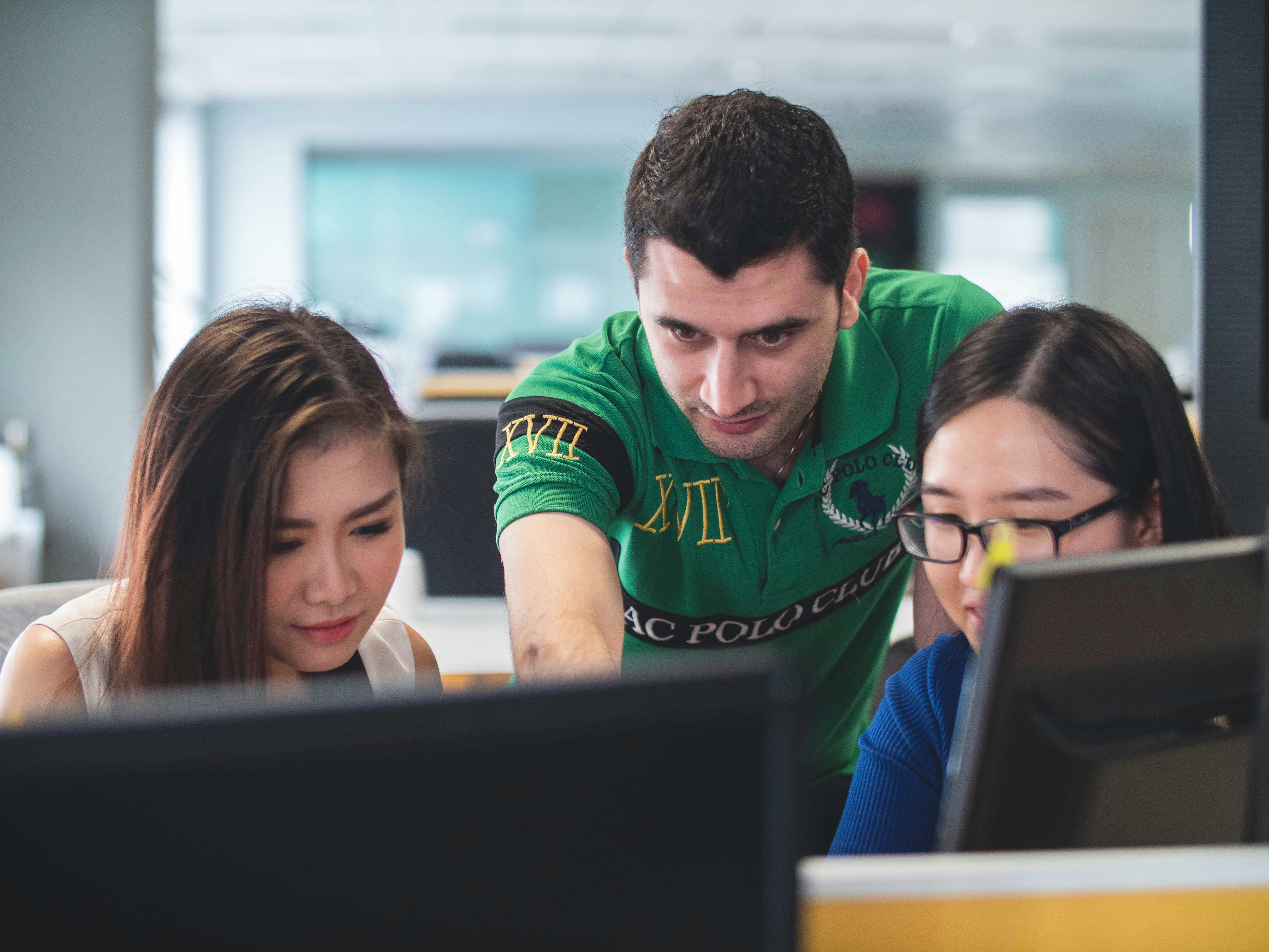 Three people stand over a pair of computer monitors, looking intently at the screen. 