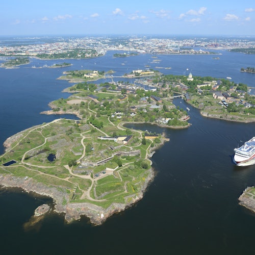 Aerial view of archipelago with green islands, buildings, pathways, and a large cruise ship docked near the shoreline.