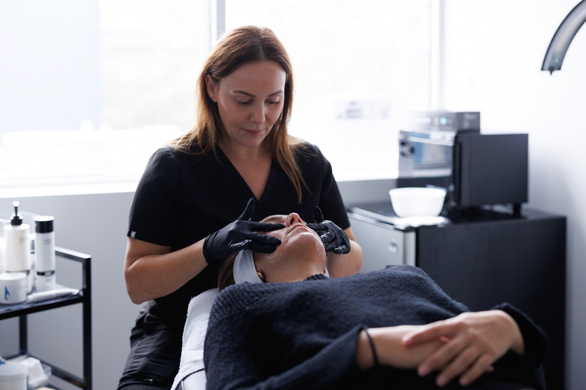 Patiente lors d'un traitement de microneedling. Couchée surl e dos avec l'esthéticienne ayant les mains sur son visage.