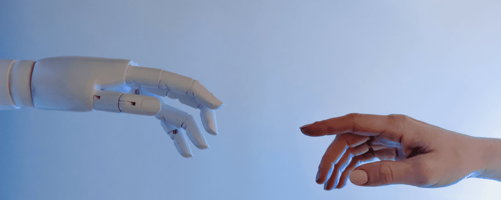 A robotic hand reaches toward a human hand against a soft blue background, symbolizing connection between technology and humanity.