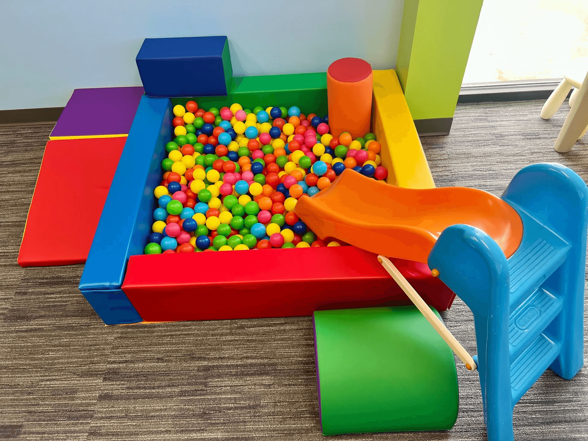 Pediatric physical therapy area showing a colorful ball pit and foam stairs designed for children's sensory and motor skill development.