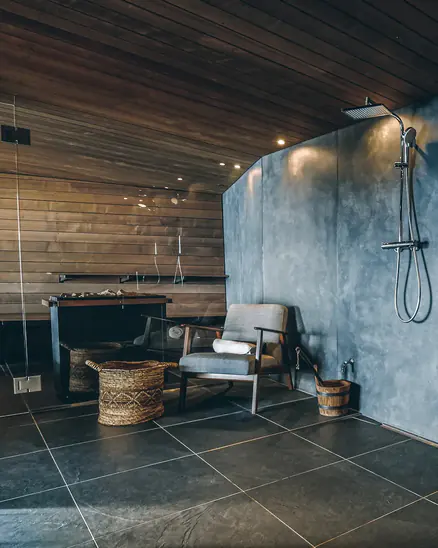 Saunavorraum mit Betonwand, Regendusche, Sessel und schwarzen Bodenfliesen