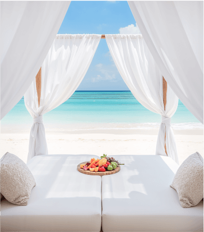 Canopy bed with fresh fruit platter facing a serene turquoise beach and blue sky.