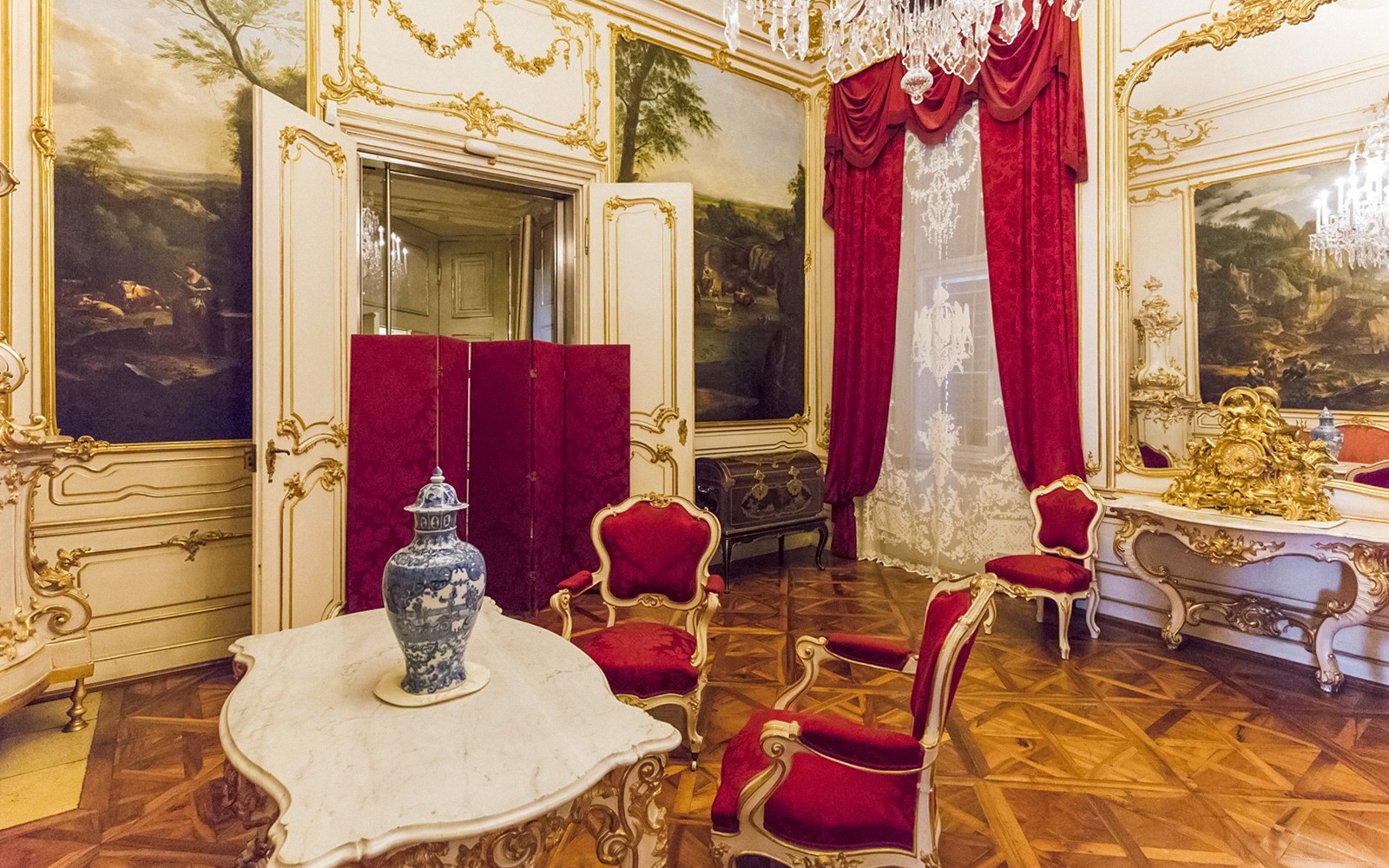 Interior Istana Schönbrunn dengan kursi merah mewah, meja marmer, dan vas dekoratif.