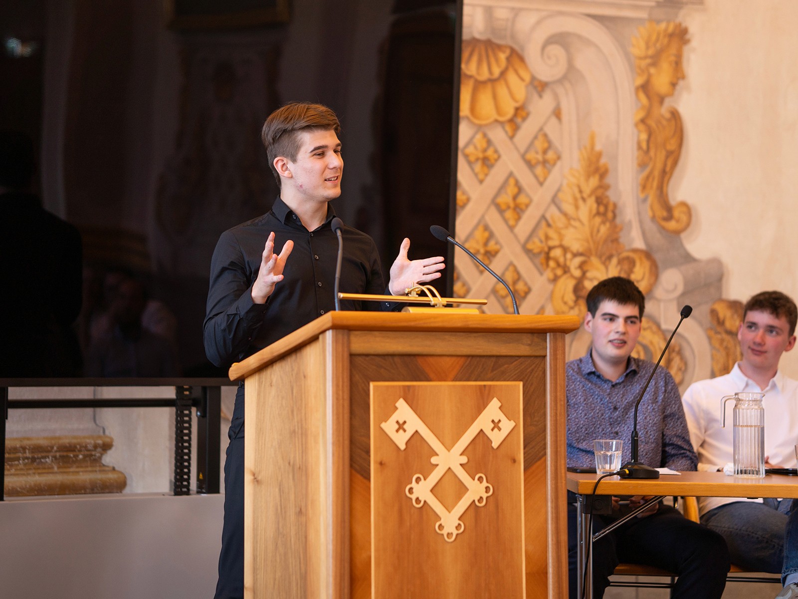 Schüler präsentiert Argumente am Rednerpult der Debattenschmiede mit gestikulierender Rhetorik.
