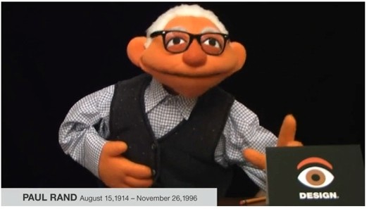 A photo of a poppet portraying an old man with a card with an eye and word design in front of it.