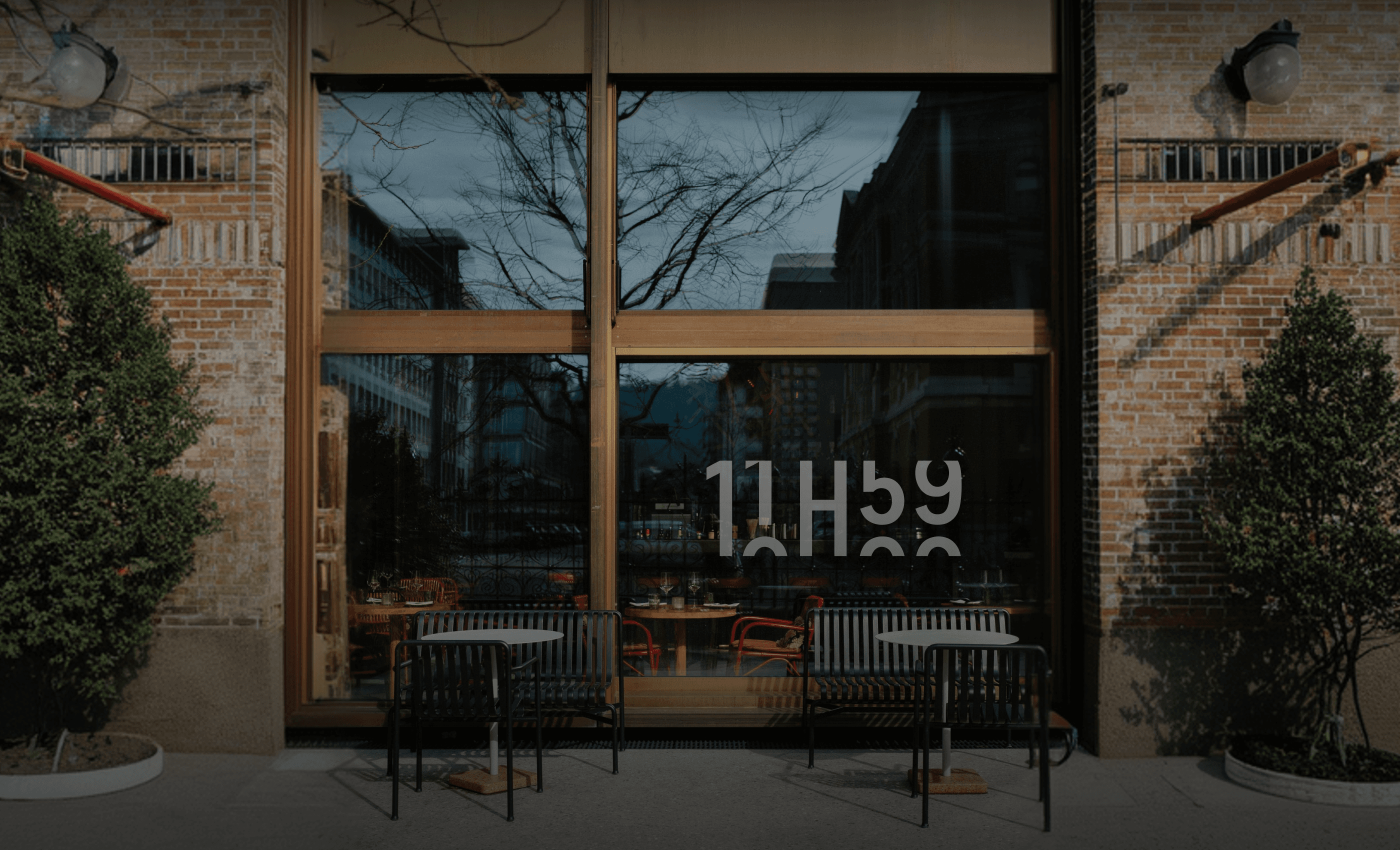 Façade d'un restaurant moderne avec de grandes vitres, des briques rouges et une terrasse extérieure avec des tables noires.